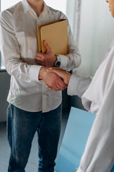 Two colleagues in casual office attire shaking hands, symbolizing a professional agreement.