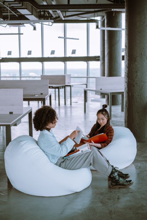 Free Two employees read on bean bags in a modern office with large windows. Stock Photo
