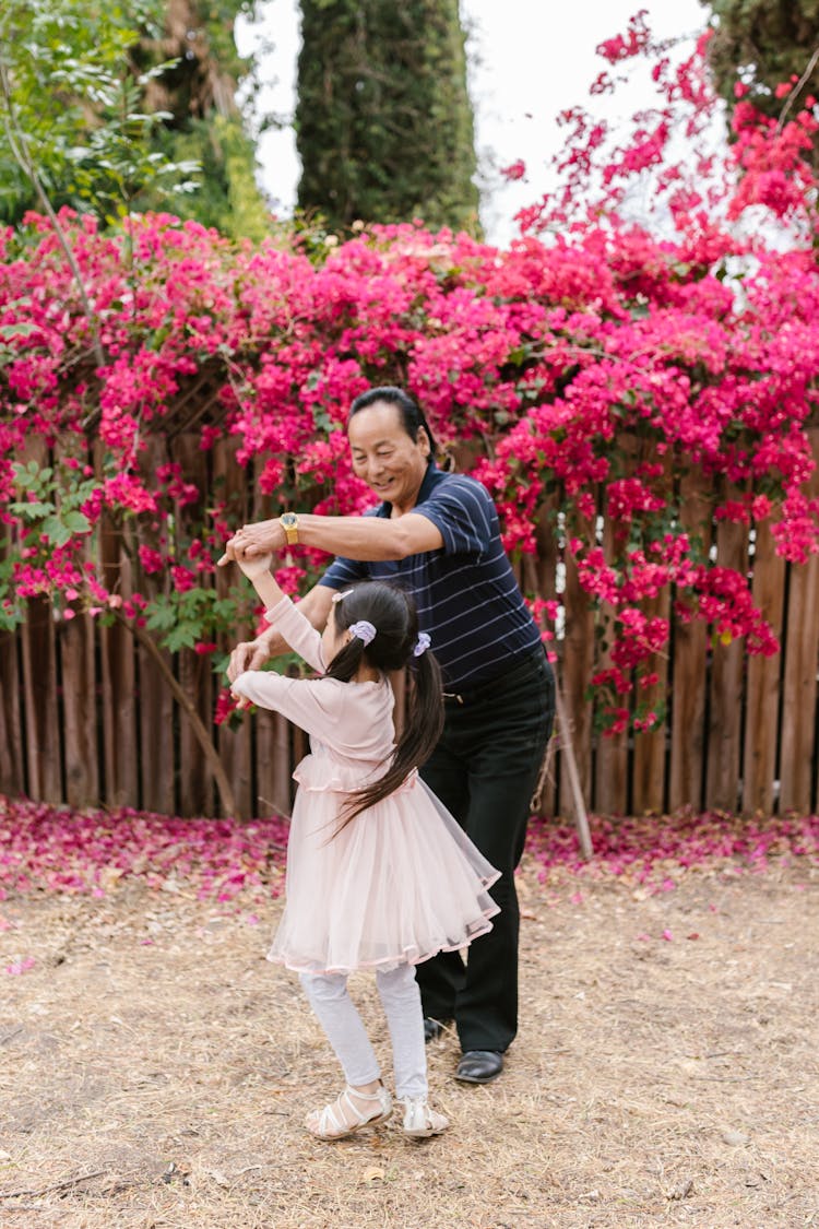 A Girl Wearing A Pink Dress Dancing With An Elderly Man In Striped Shirt