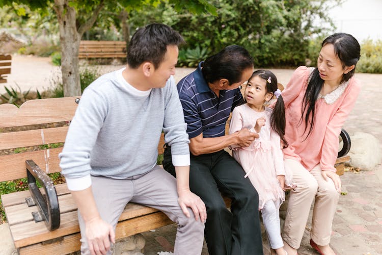 A Family Sitting On A Bench At A Park