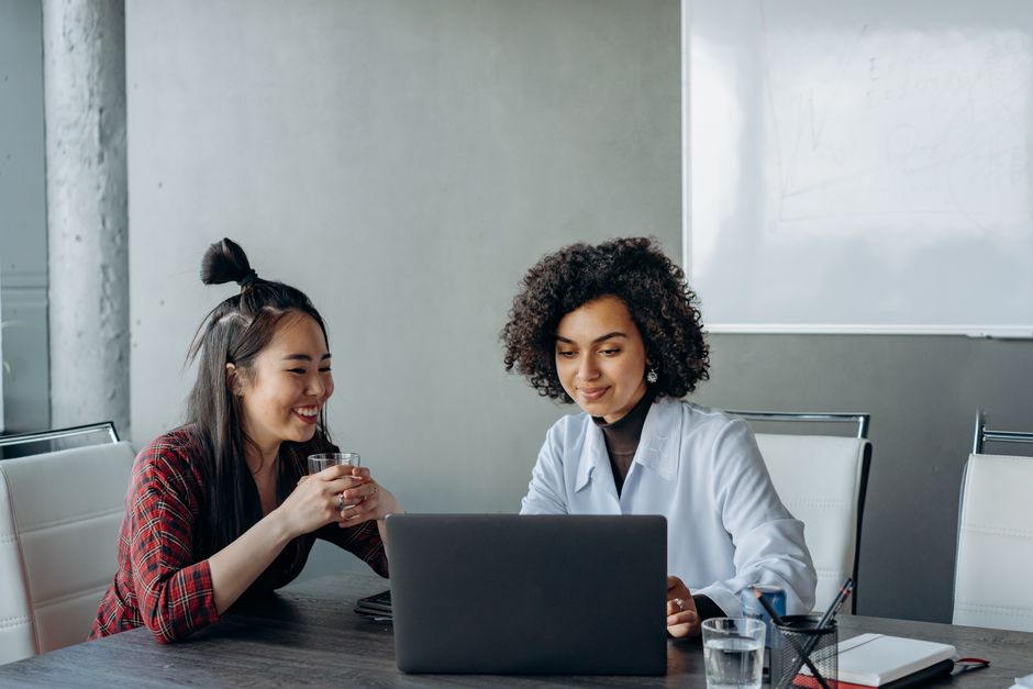 Asian and black women working together on a laptop in an office setting.