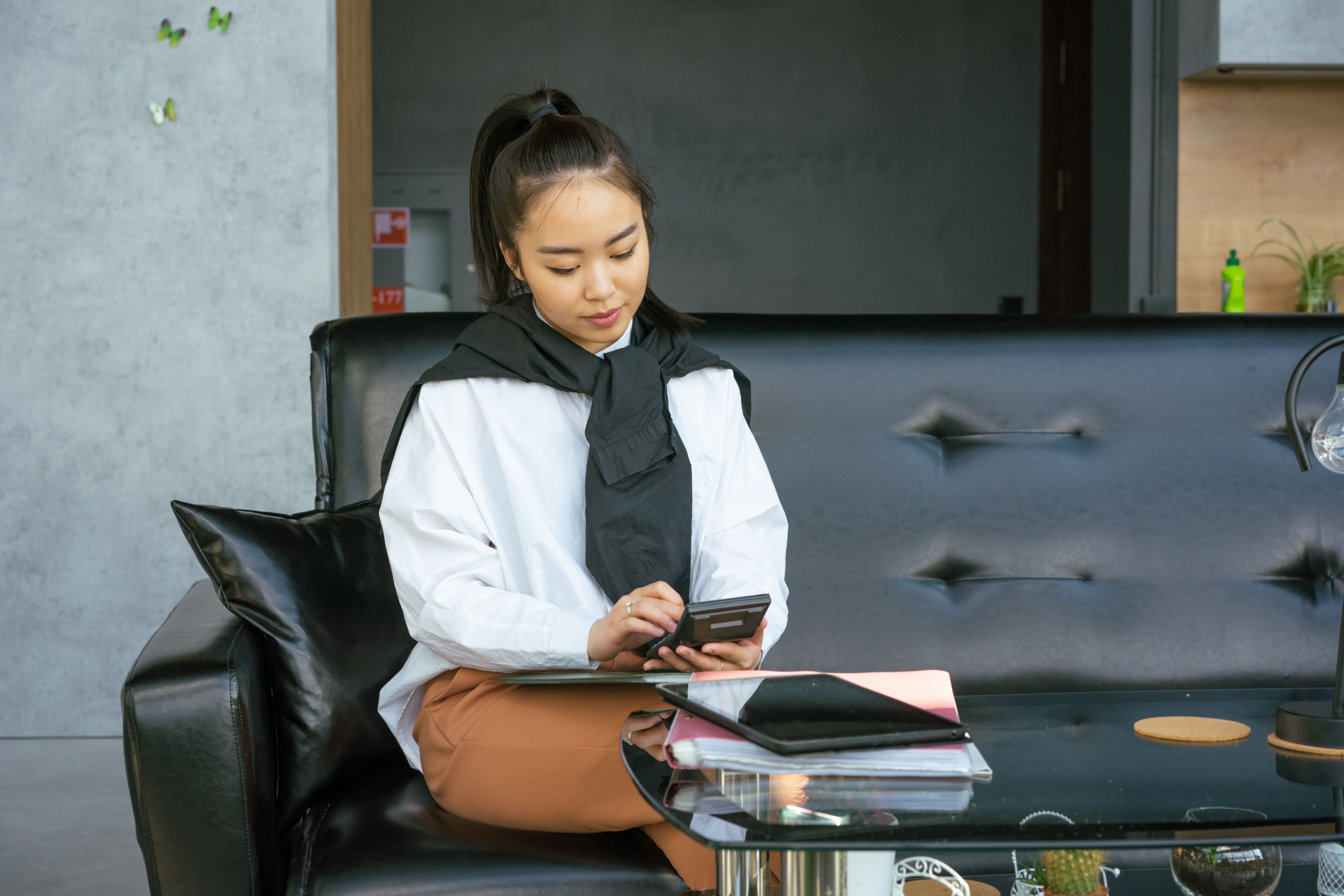 Asian woman using smartphone and planner in a modern office setting.