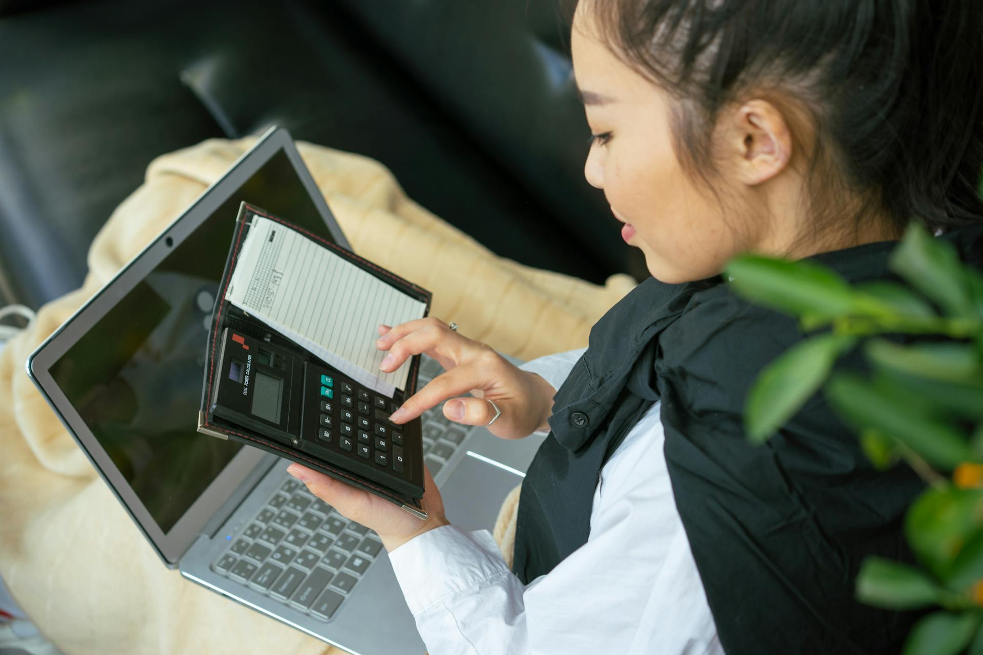 Focused young woman calculating finances on laptop indoors.