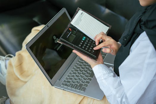 Close-up of a person using a calculator with a laptop, symbolizing home office productivity.
