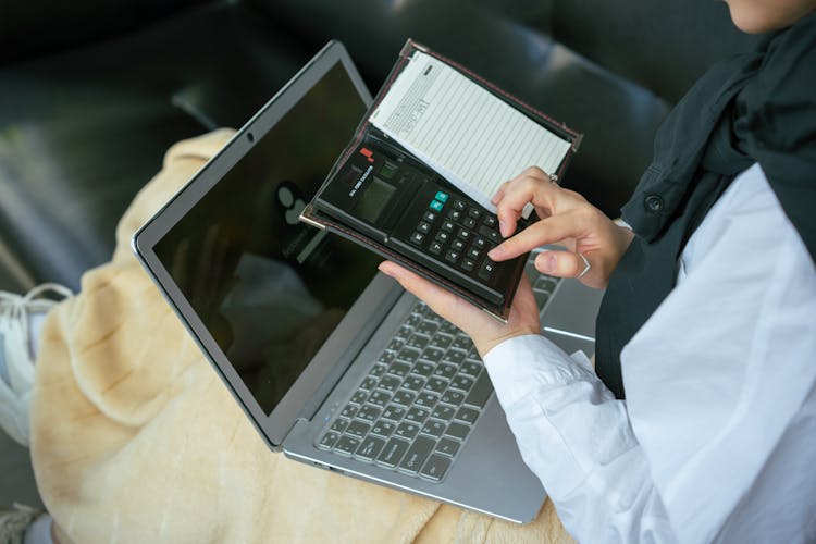 A Person With Laptop On Her Computing Something On The Calculator