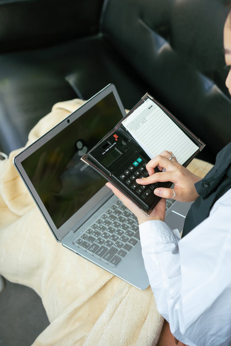 A Woman Using A Calculator While Having A Laptop On Her Lap