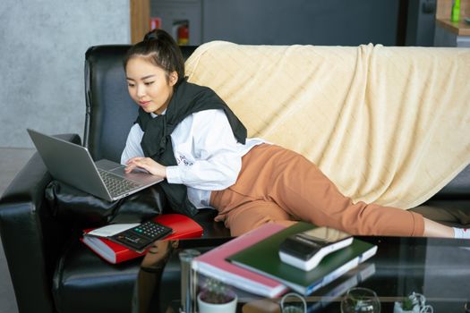 Young woman in casual wear browsing laptop while lying on couch indoors.