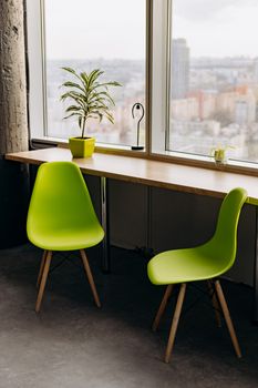 A sleek minimalist office space featuring green chairs, wooden desk, and a cityscape window view.
