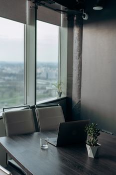 A sleek office setting with a laptop, glass, and potted plant by a window overlooking the city.