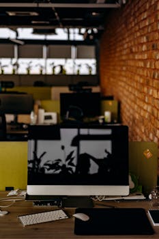 A sleek modern office featuring a desktop computer on a desk against a brick wall.