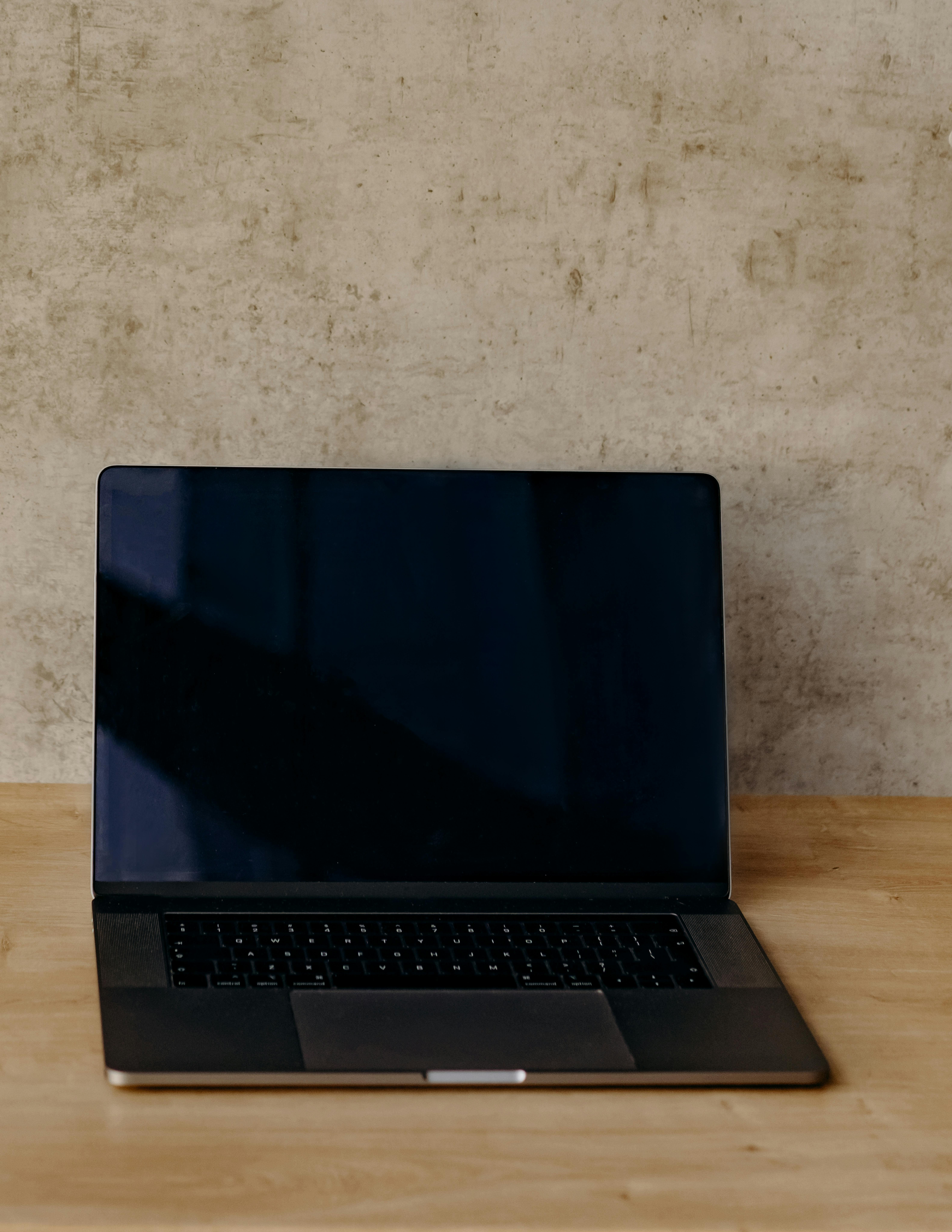 Free Open laptop on a wooden desk against a textured wall, perfect for tech and work themes. Stock Photo