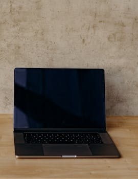 Open laptop on a wooden desk against a textured wall, perfect for tech and work themes.
