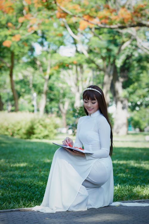 Woman Squatting on Stone Pavement Holding Notebook