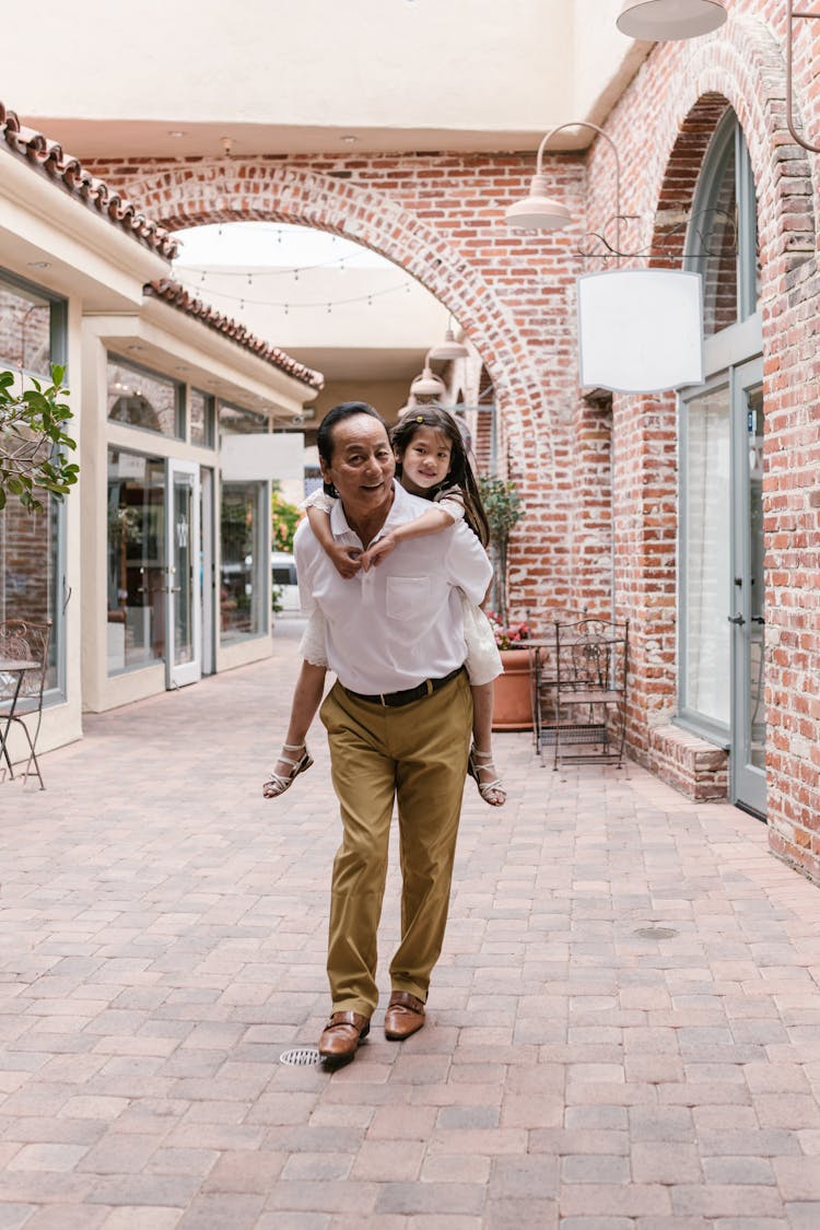 A Man In White Shirt Carrying A Girl While Walking On The Street