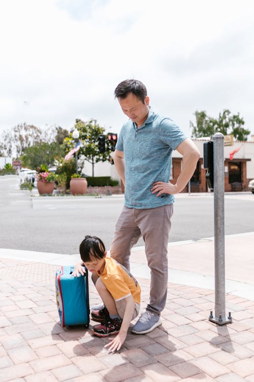 A Father Standing Beside the Boy Picking Something on the Ground