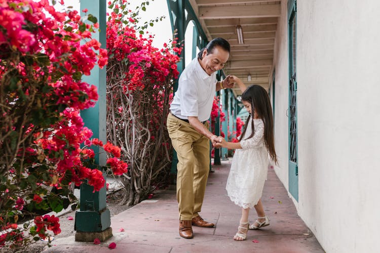 Granddaughter And Grandfather Dancing On The Hallway Near Bougainvillea Flowers