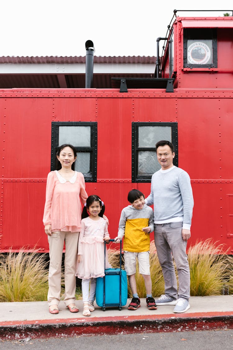 A Happy Family Standing Near The Red Train While Looking At The Camera