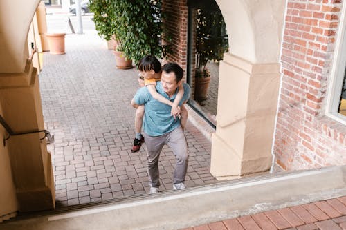 A Father Carrying His Son on His Back while Going Up the Concrete Stairs