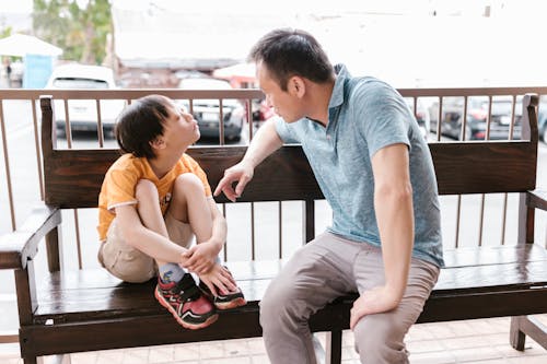 Free Father and Son Sitting on a Wooden Bench while Having a Conversation Stock Photo