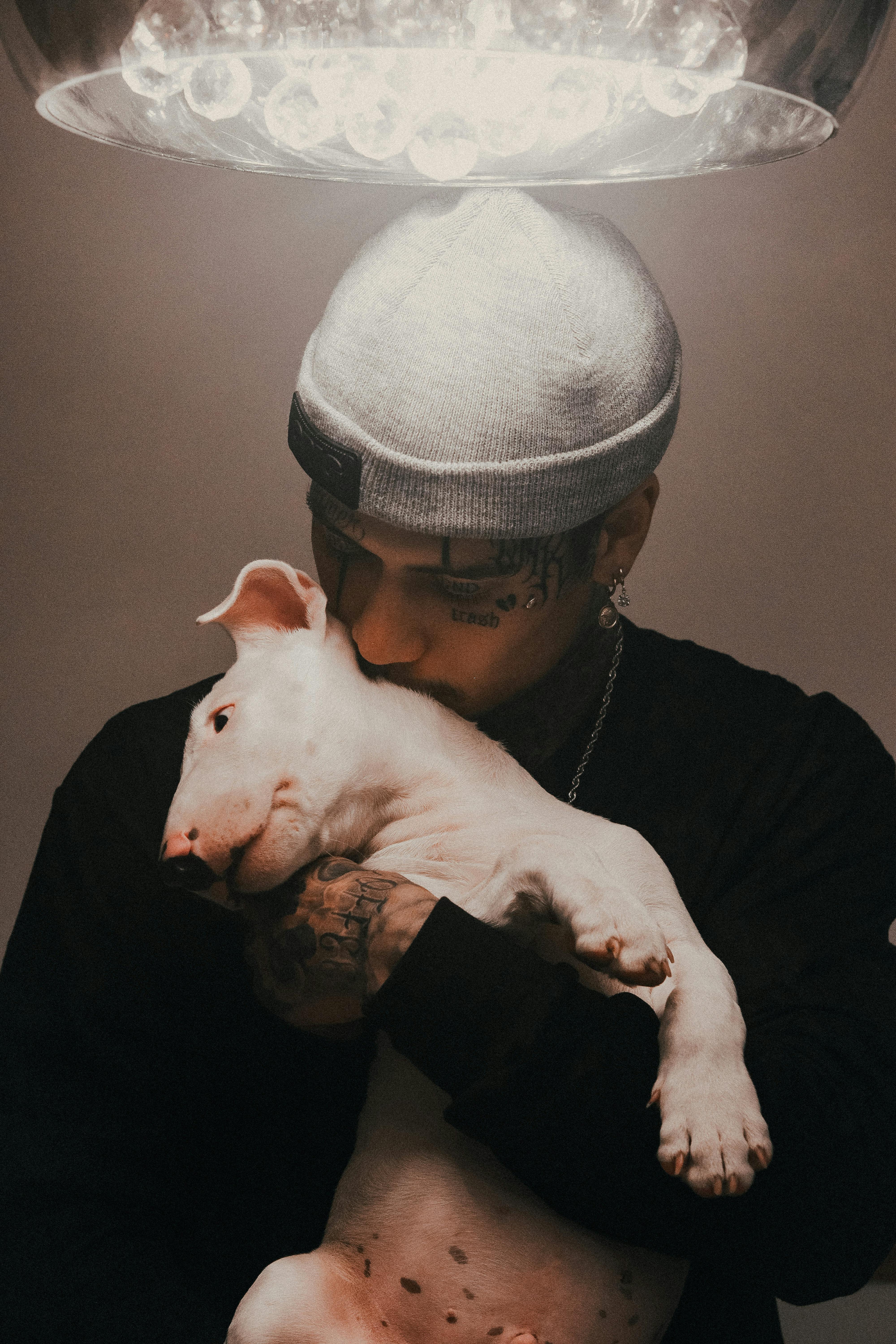 A tattooed man lovingly hugs a bull terrier puppy, showcasing affection and companionship.