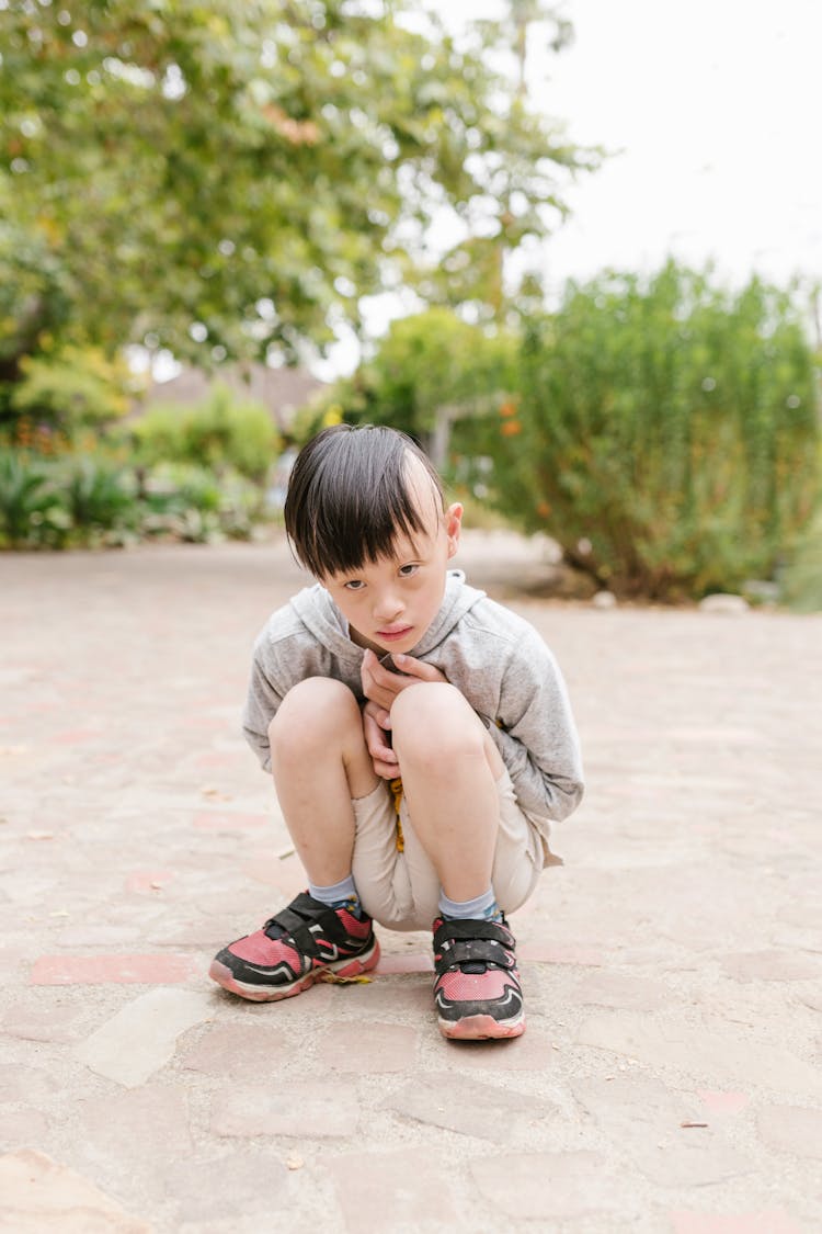 Special Child In Gray Hoodie Sitting On Pavement