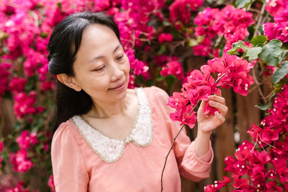 how to overcome imposter syndrome in your career - A woman admires bright pink bougainvillea flowers, creating a serene and colorful scene.