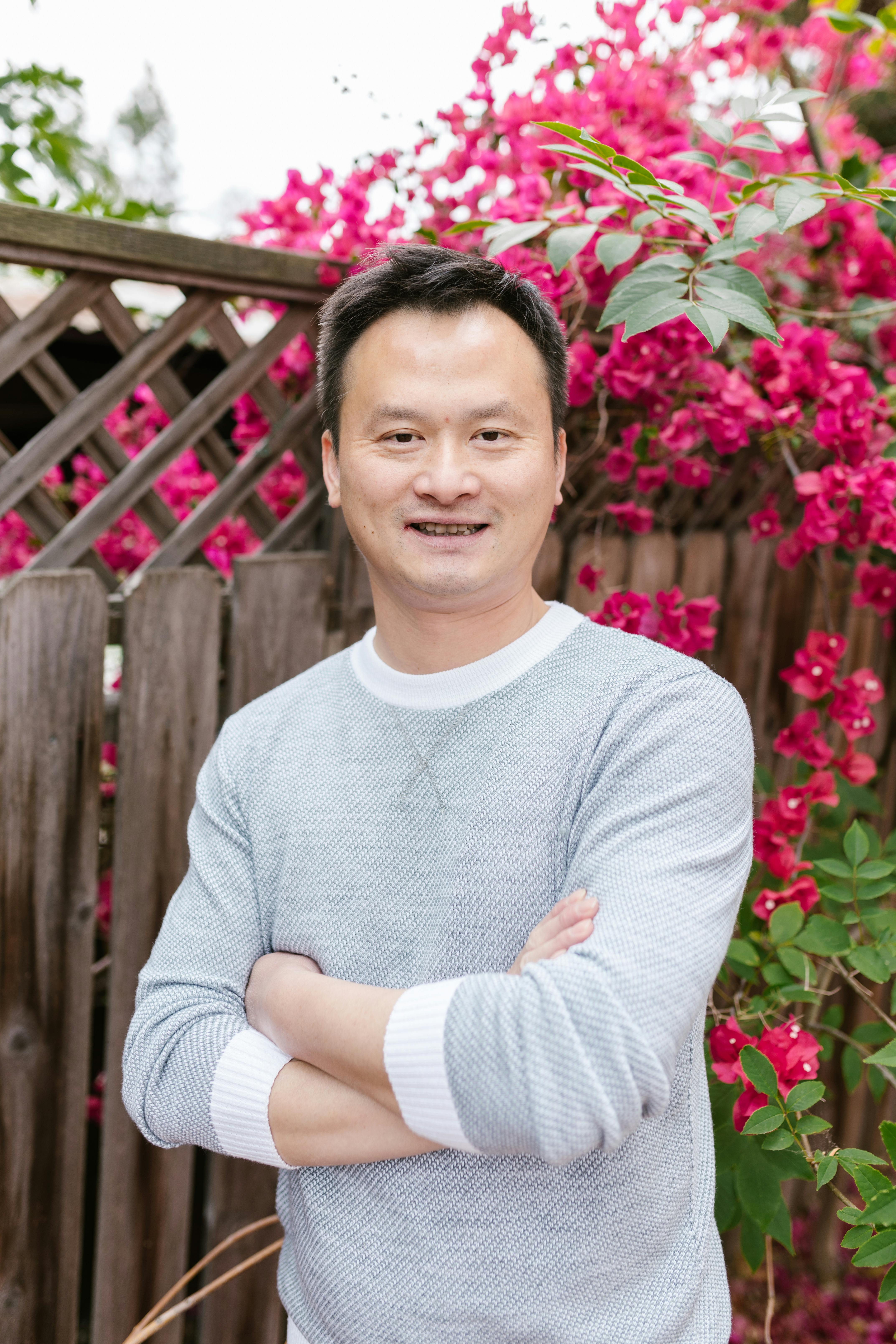 Portrait of a smiling man standing outdoors with vibrant pink bougainvillea flowers in the background.