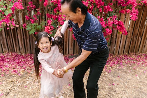 Grandfather and Granddaughter Playing Together Near Wooden Fence with Bougainvillea Flowers