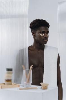 Black man with eye patches and towel, engaging in a minimalist skincare routine.