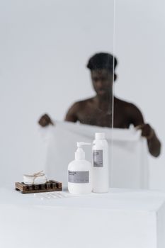 Adult man drying off after shower with body care products in a minimalist bathroom setting.
