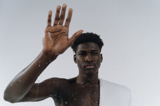Adult black man with towel touching glass, creating a modern and reflective mood indoors.