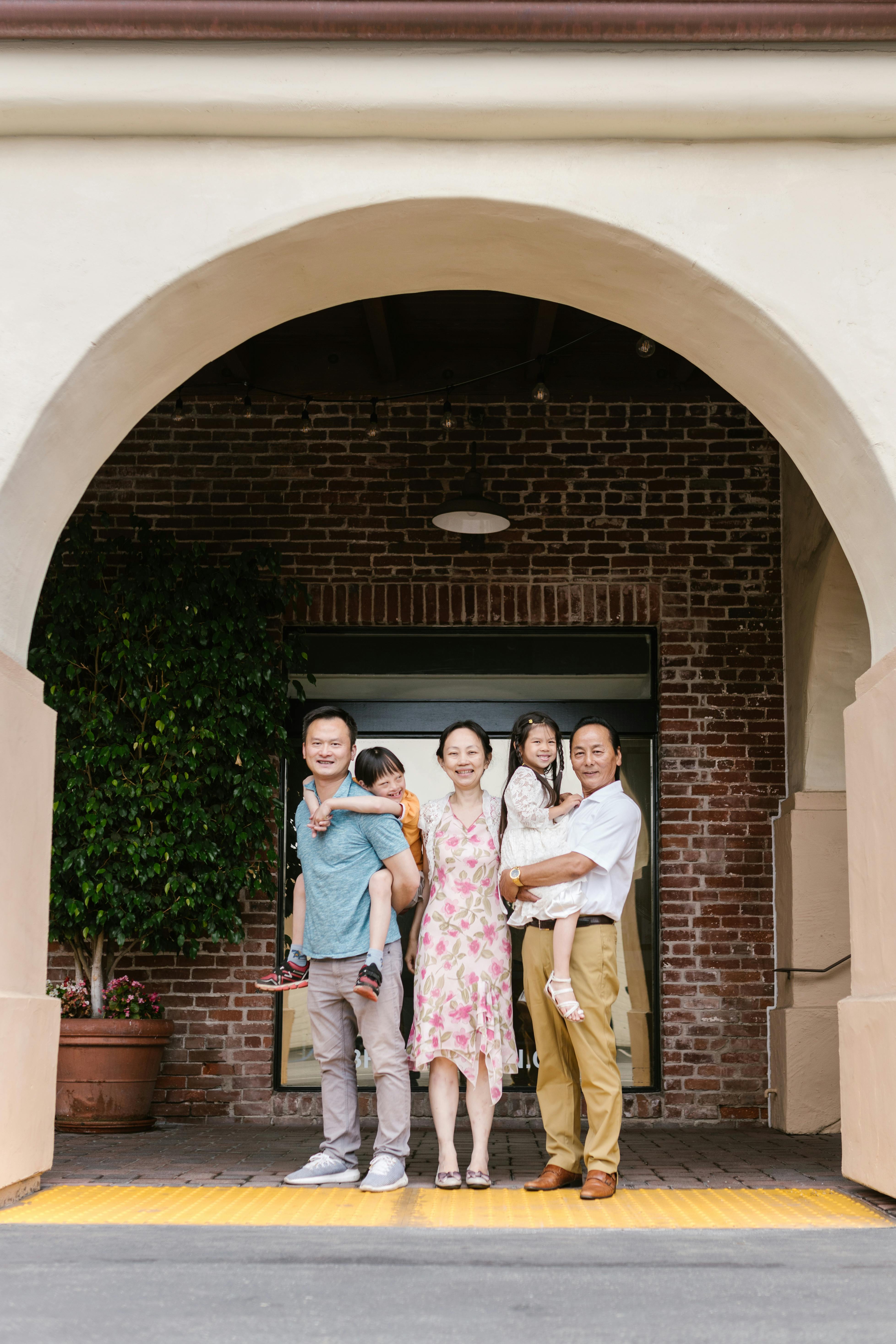 A joyful Asian family of four poses under a scenic archway outdoors.