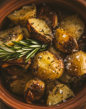 Savor the close-up view of herb-roasted potatoes in a terracotta dish, adorned with aromatic rosemary sprigs.