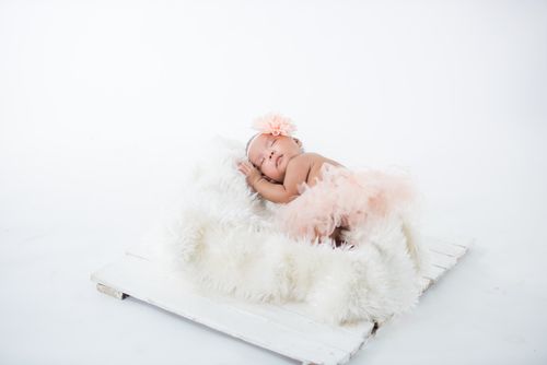 Free A serene scene of a baby sleeping on a white furry rug in a photography studio setting. Stock Photo