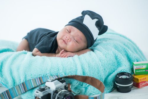 Free Cute sleeping baby with camera gear on a cozy blanket in a studio setting. Perfect for newborn photography themes. Stock Photo