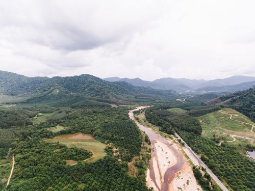Free Aerial shot showcasing lush green landscapes, winding river, and distant mountain range under a cloudy sky. Stock Photo