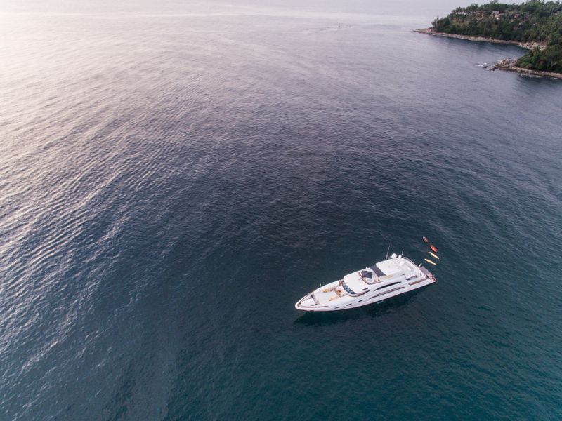 Aerial view of a luxury yacht anchored in calm waters near a rocky island shore