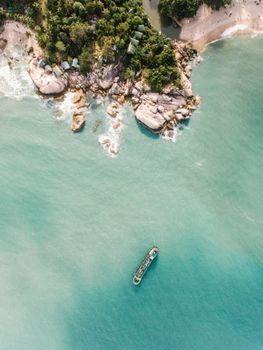 Drone shot of a tropical coastline with a lone boat in turquoise waters.