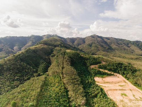 Free A breathtaking aerial shot showcasing lush hills and valleys under a cloud-speckled sky. Stock Photo