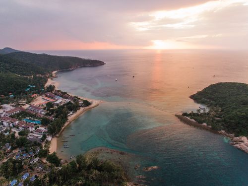 Free Stunning aerial view of a tropical beach with lush greenery and calm waters during a sunset. Stock Photo