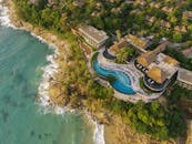 令人惊叹的海滨度假村鸟瞰图，设有被郁郁葱葱的绿色植物包围的豪华无边泳池