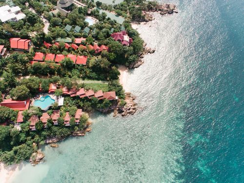 Free A stunning aerial shot of a tropical coastline featuring villas, lush greenery, and clear ocean waters. Stock Photo