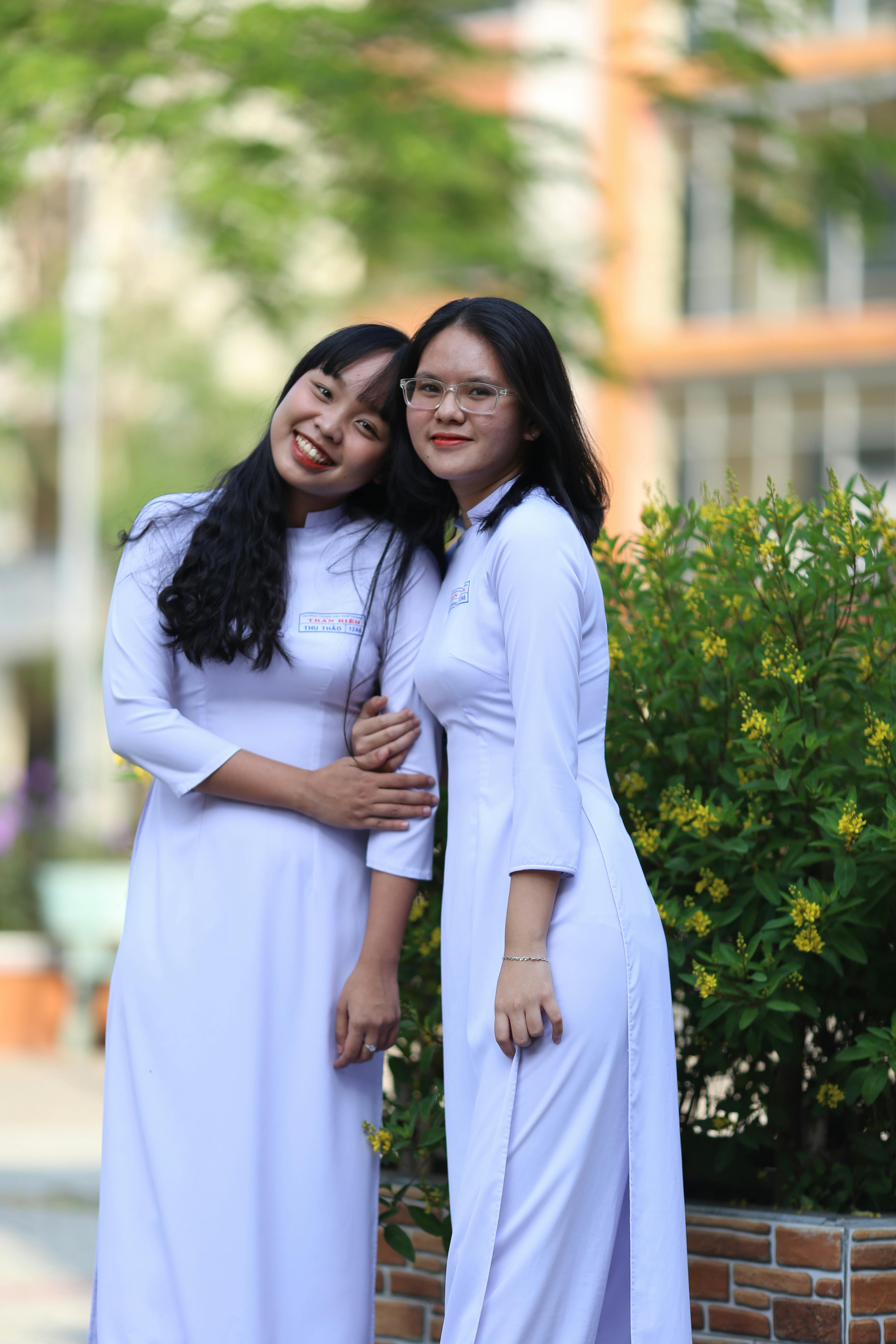 photograph of girls in white dress standing near yellow flowers