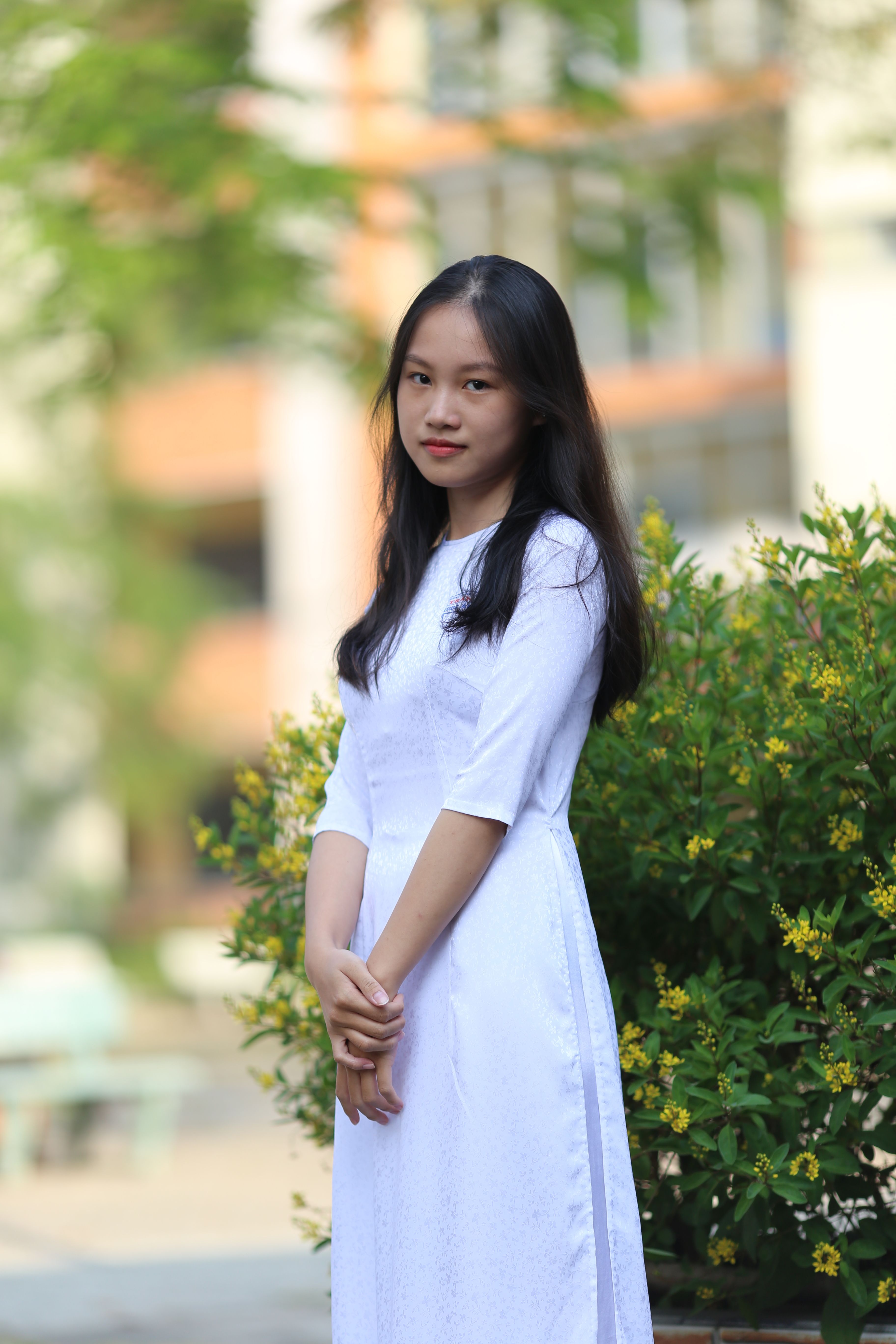 Elegant young woman in white dress posing in a lush outdoor setting.
