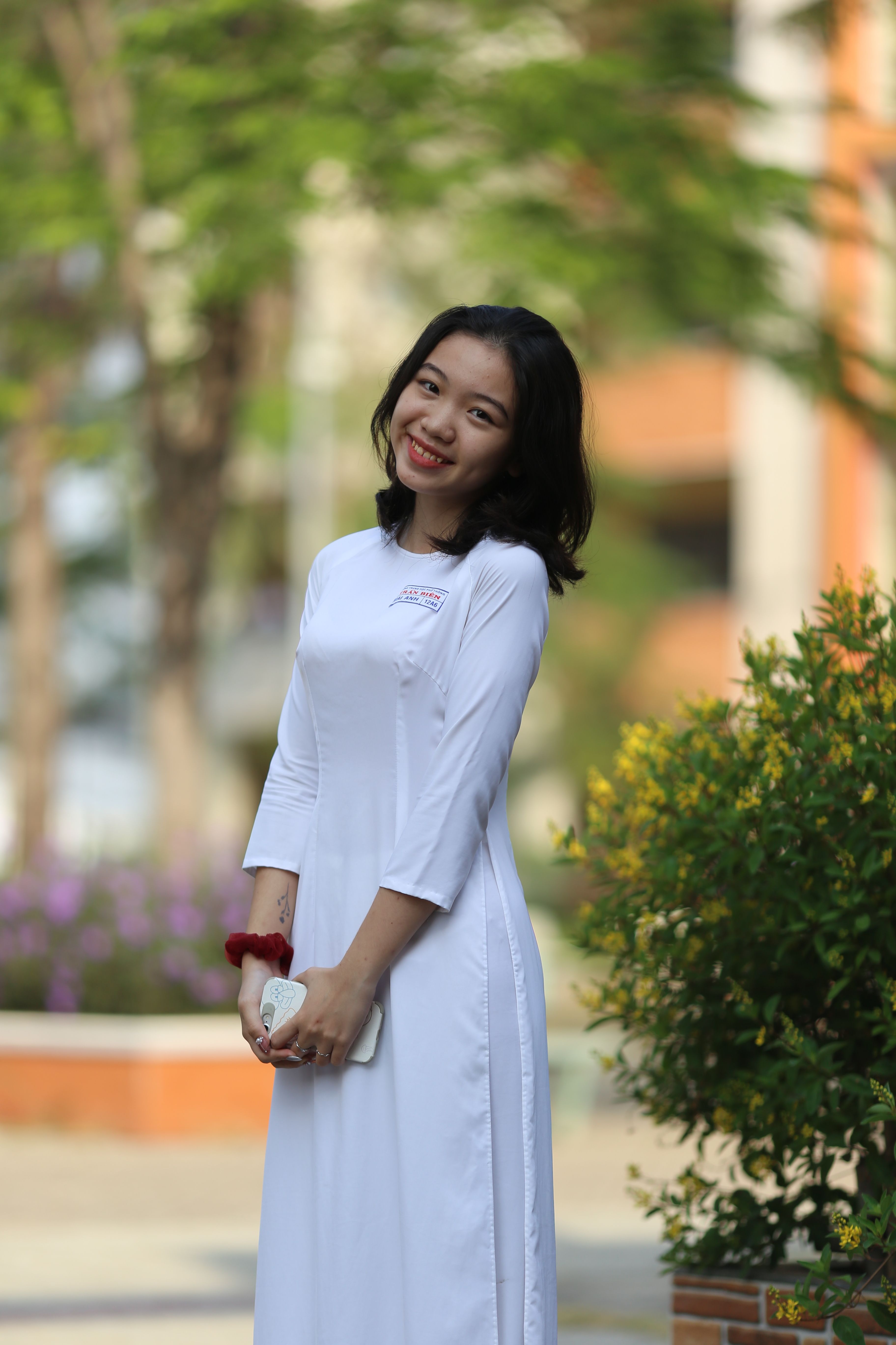 Cheerful young woman in traditional white dress smiling while standing outdoors in a natural setting.