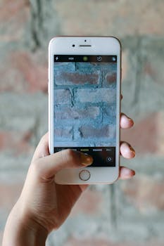 A hand holding a smartphone with a close-up image of a brick wall on the screen.