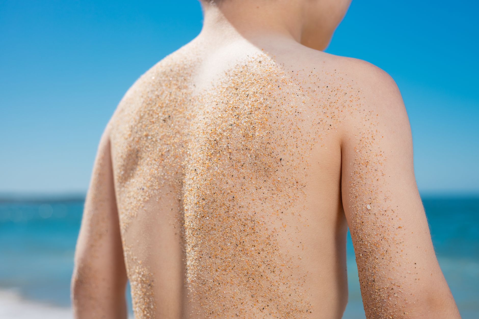 Vitamin D3 benefits — A child's sand-covered back at the beach under a bright blue sky, capturing a summer vibe.