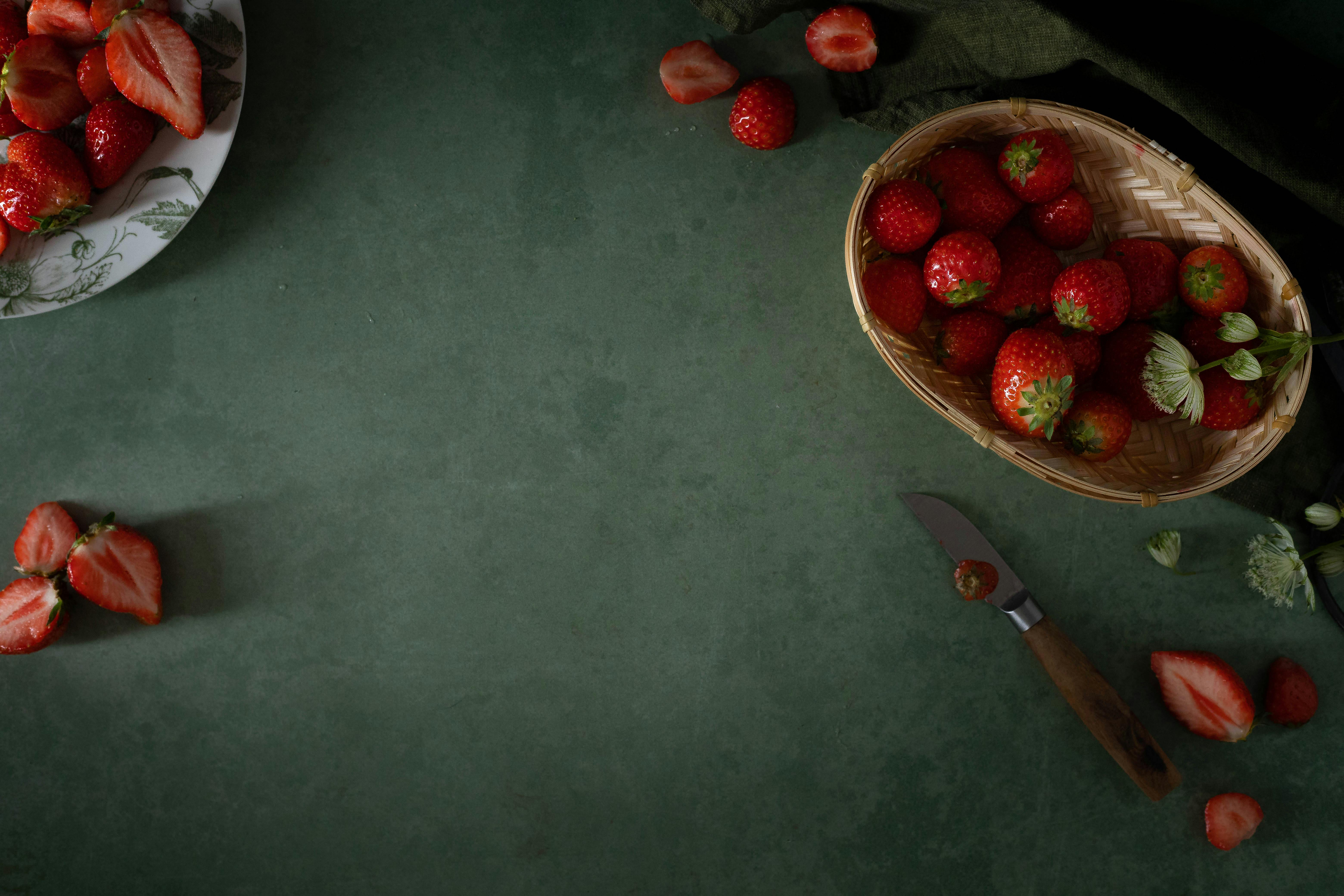 Overhead view of strawberries on a green background with a rustic knife, showcasing fresh fruit arrangement.