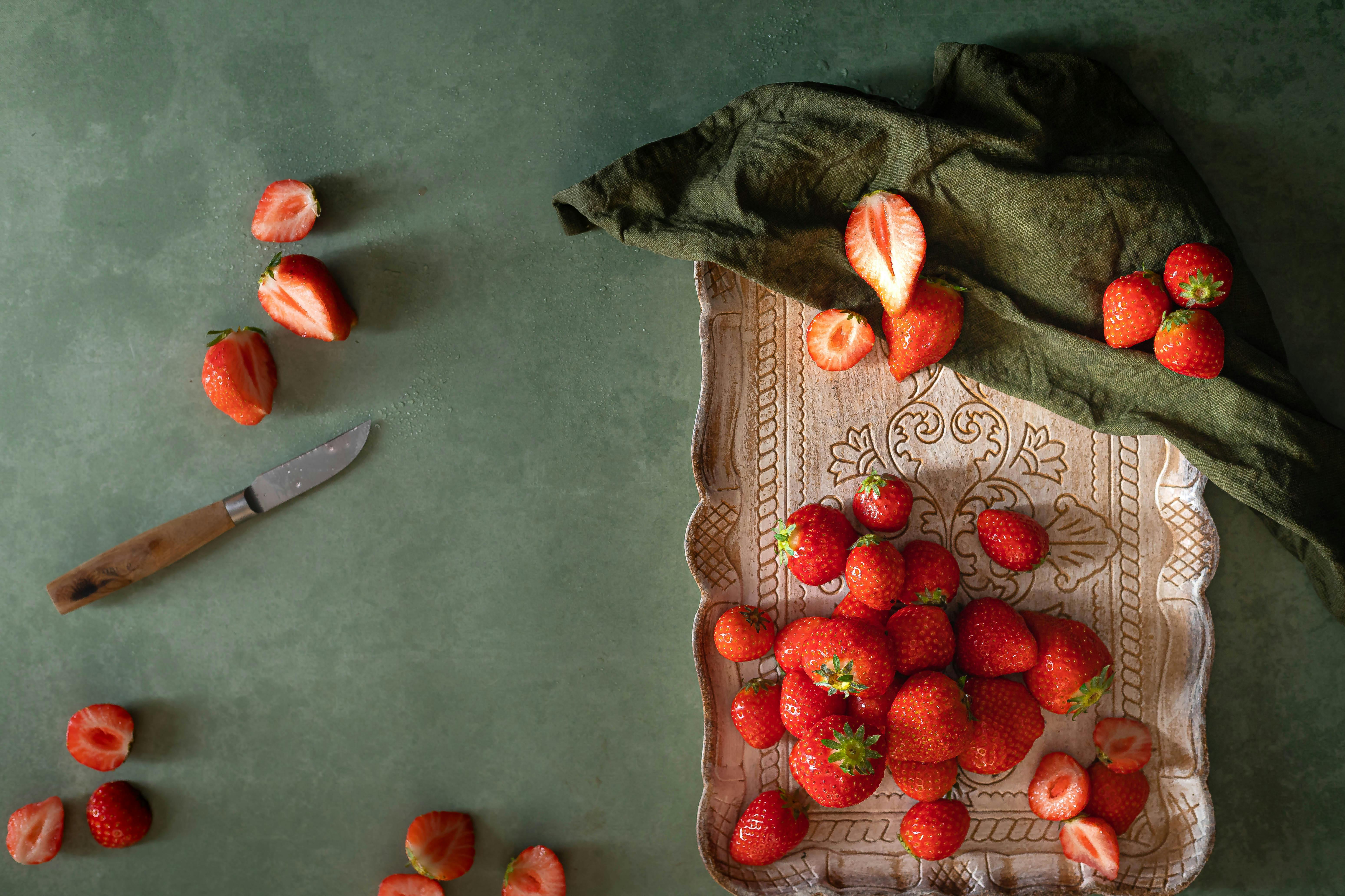 Top-down view of strawberries arranged on a tray with scattered slices and a knife.