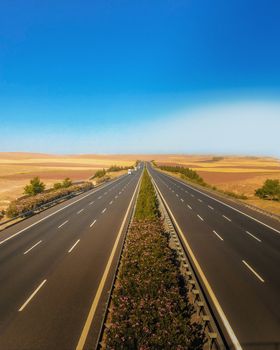 Aerial view of a symmetrical highway stretching through a desert landscape under a bright blue sky.